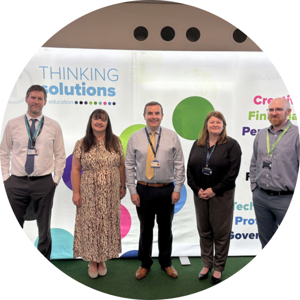 Five people stand in front of a “Thinking Solutions Education” banner, posing for a group photo indoors and showcasing their commitment to thinking solutions for education.